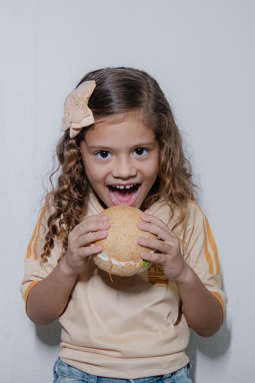 Criança sorrindo e segurando um hambúrguer do Meu Burguer