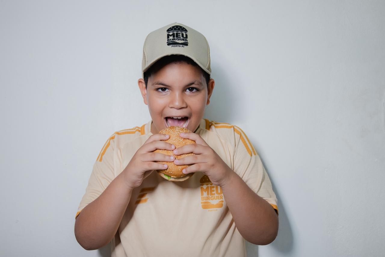 Criança com boné do Meu Burguer prestes a morder um hambúrguer